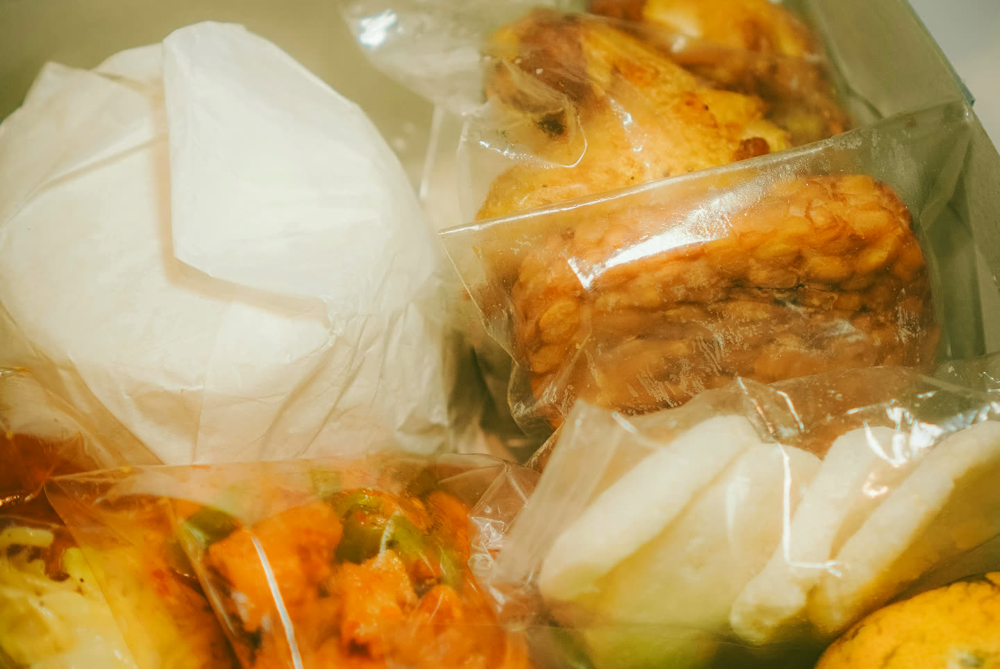An open nasi kotak: rice, fried chicken, tempeh, crackers, pickles and an orange